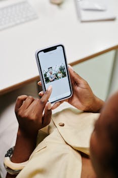 Close-up of hands using a smartphone to browse photos at a desk.