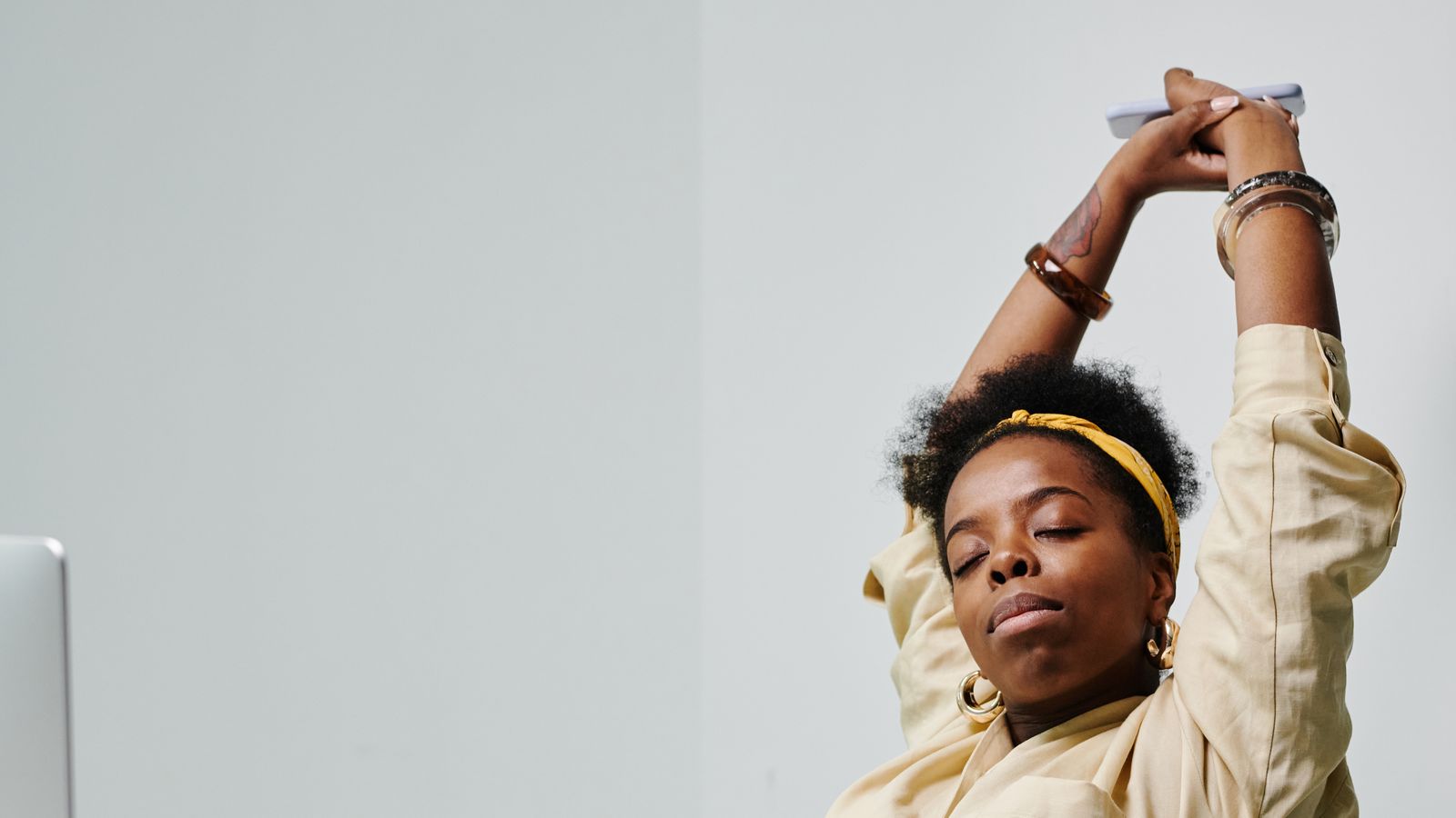 A woman stretching with her eyes closed at an office desk