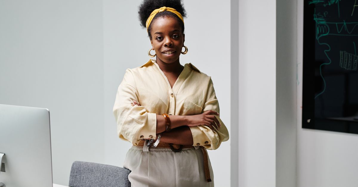 Confident black woman with curly hair and headwrap smiling in a modern office environment.