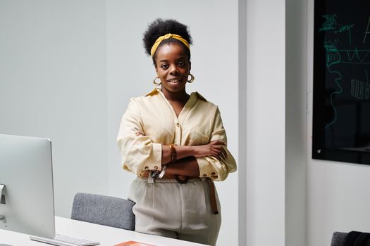 Confident black woman with curly hair and headwrap smiling in a modern office environment.