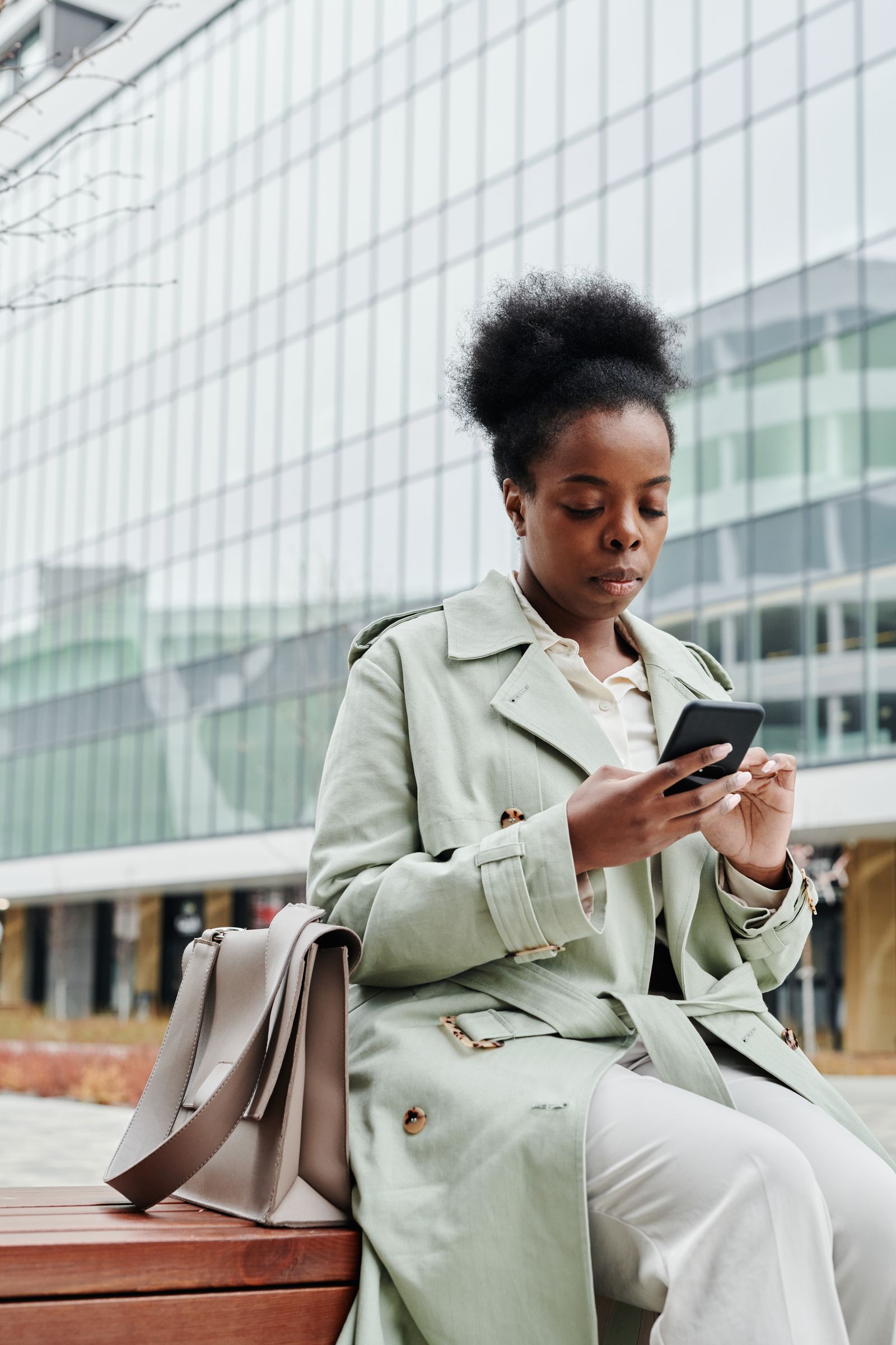 Woman in a trench coat checking her smartphone outside a modern building Woman in a trench coat checking her smartphone outside a modern building