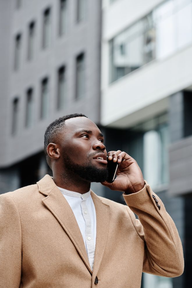 Investor in a camel coat taking a call outside an office building — photo by Darlene Alderson on Pexels