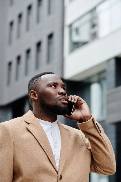 Free Urban professional in beige coat using smartphone outdoors. Stock Photo