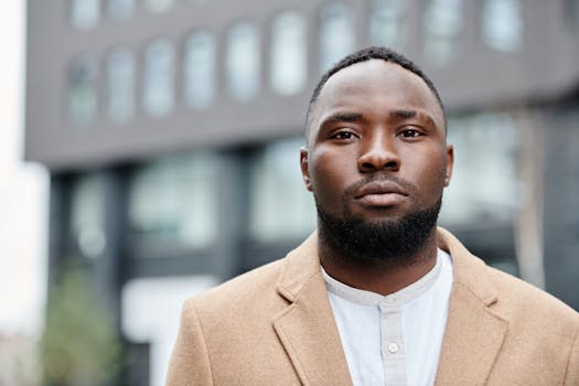 Portrait of a confident black man in a stylish coat, facing camera with urban backdrop.