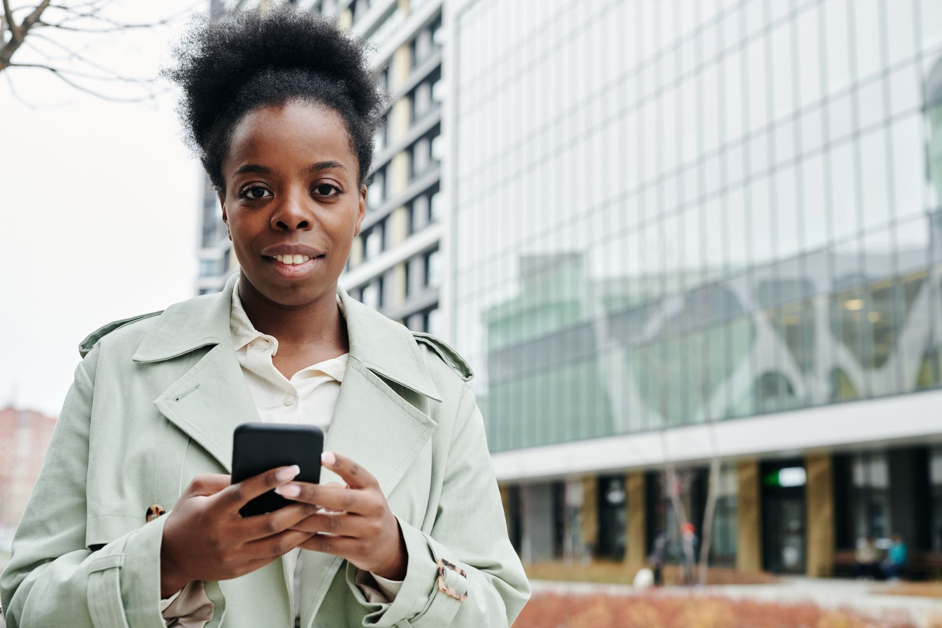 Confident black woman in business attire using smartphone outside modern office building.
