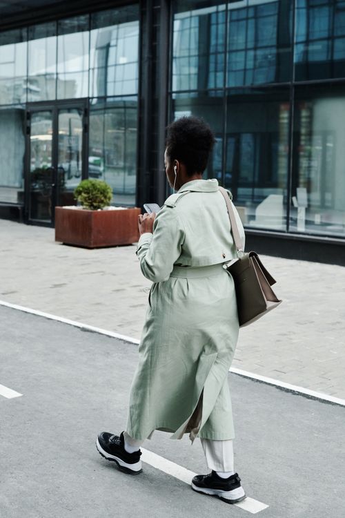 Free A stylish woman wearing headphones walks along a modern city sidewalk. Stock Photo