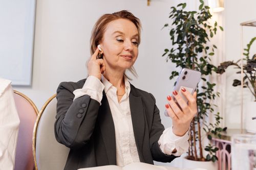 Free Businesswoman using smartphone and earbud in a meeting setting, exuding professionalism. Stock Photo