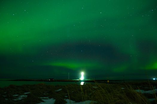 A stunning view of the aurora borealis illuminating the night sky above a coastal lighthouse.