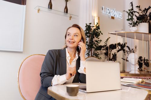 Free Businesswoman in office, speaking on phone, smiling, with laptop. Stock Photo
