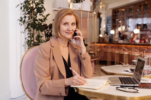 Free Professional woman multitasking with phone and notebook in a chic café setting. Stock Photo