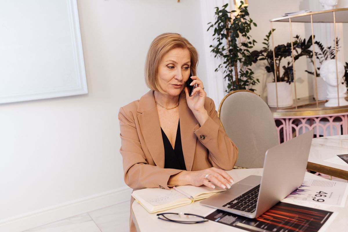 Office coordinator talking to a customer by phone while using a laptop