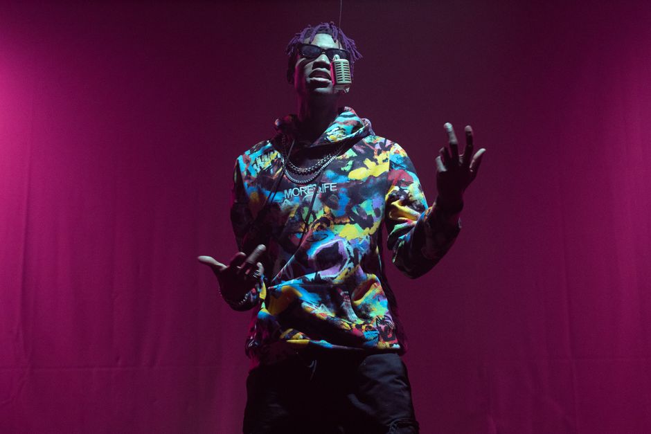 Rapper in colorful hoodie performing with mic on red stage. Captivating music and style.