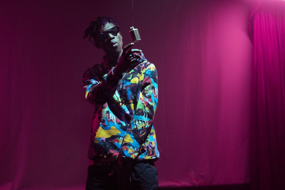 A vibrant rapper energetically performing on an indoor stage under bright lights.