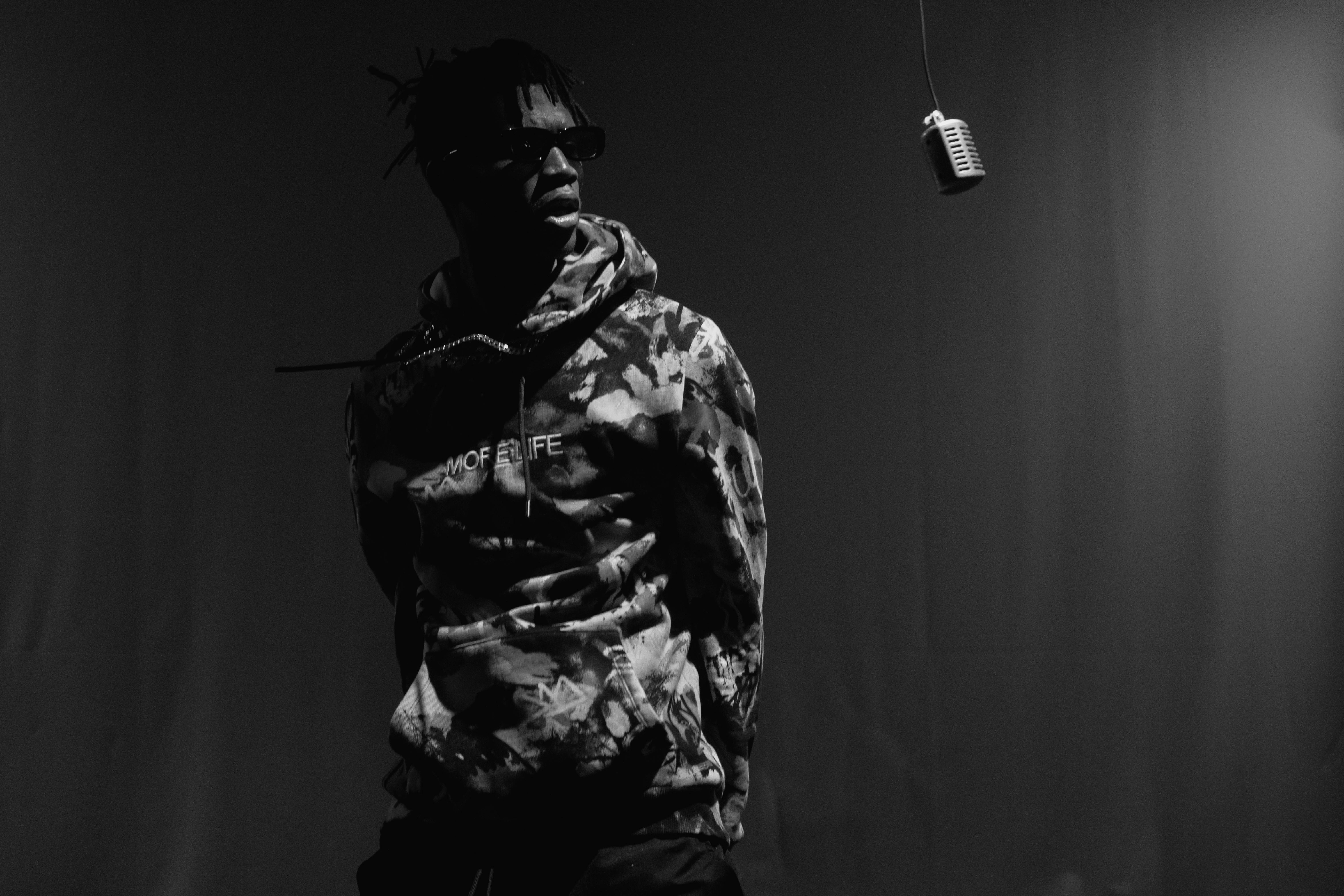 grayscale photo of a man in camouflage hoodie rapping