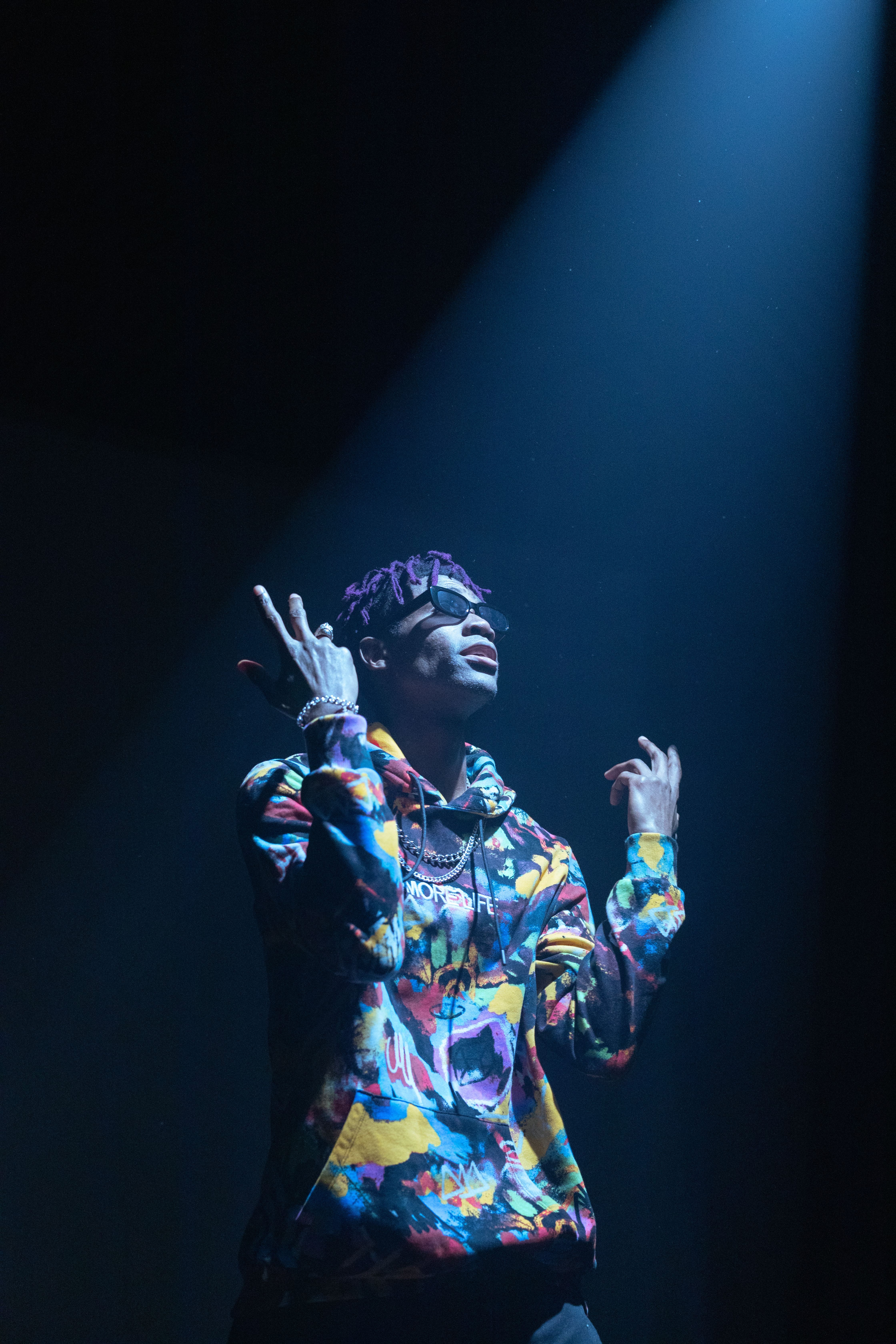 Fashionable adult man with colorful jacket stands dramatically under spotlight indoors.