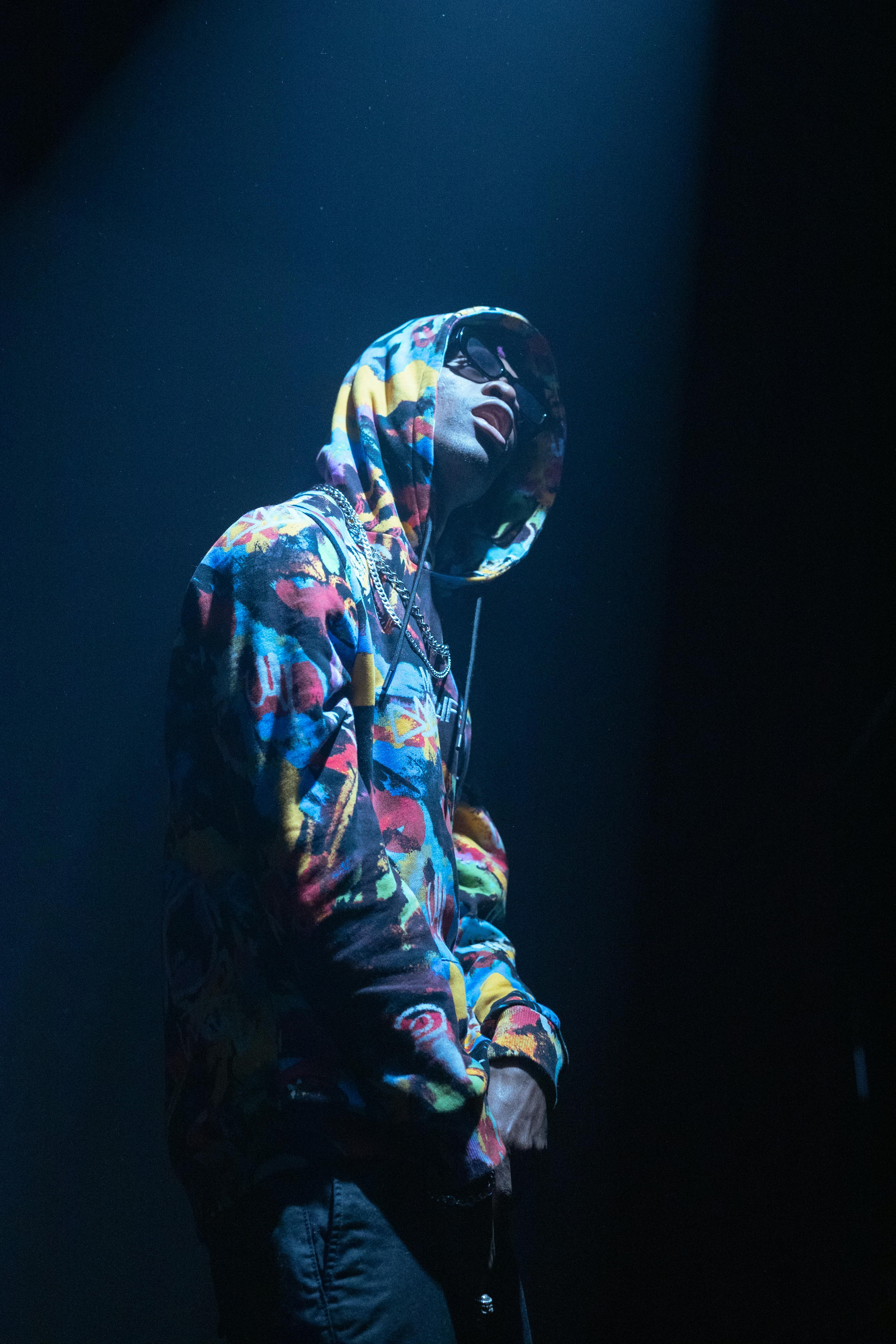 A hip hop artist in a colorful hoodie performs under a dramatic spotlight.