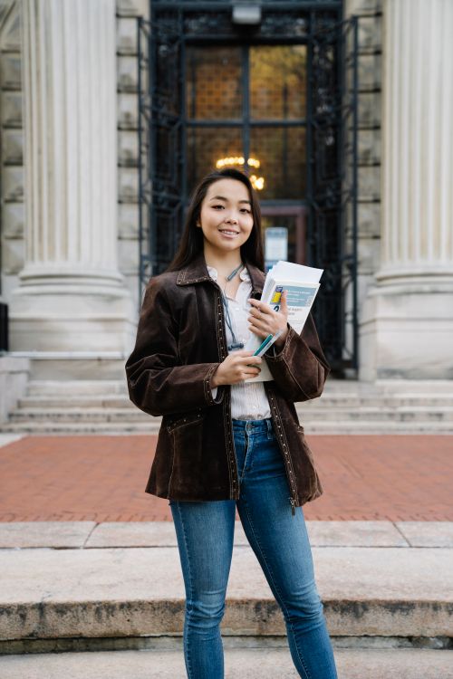 Free Confident female student holding papers in front of an ornate historic building. Stock Photo