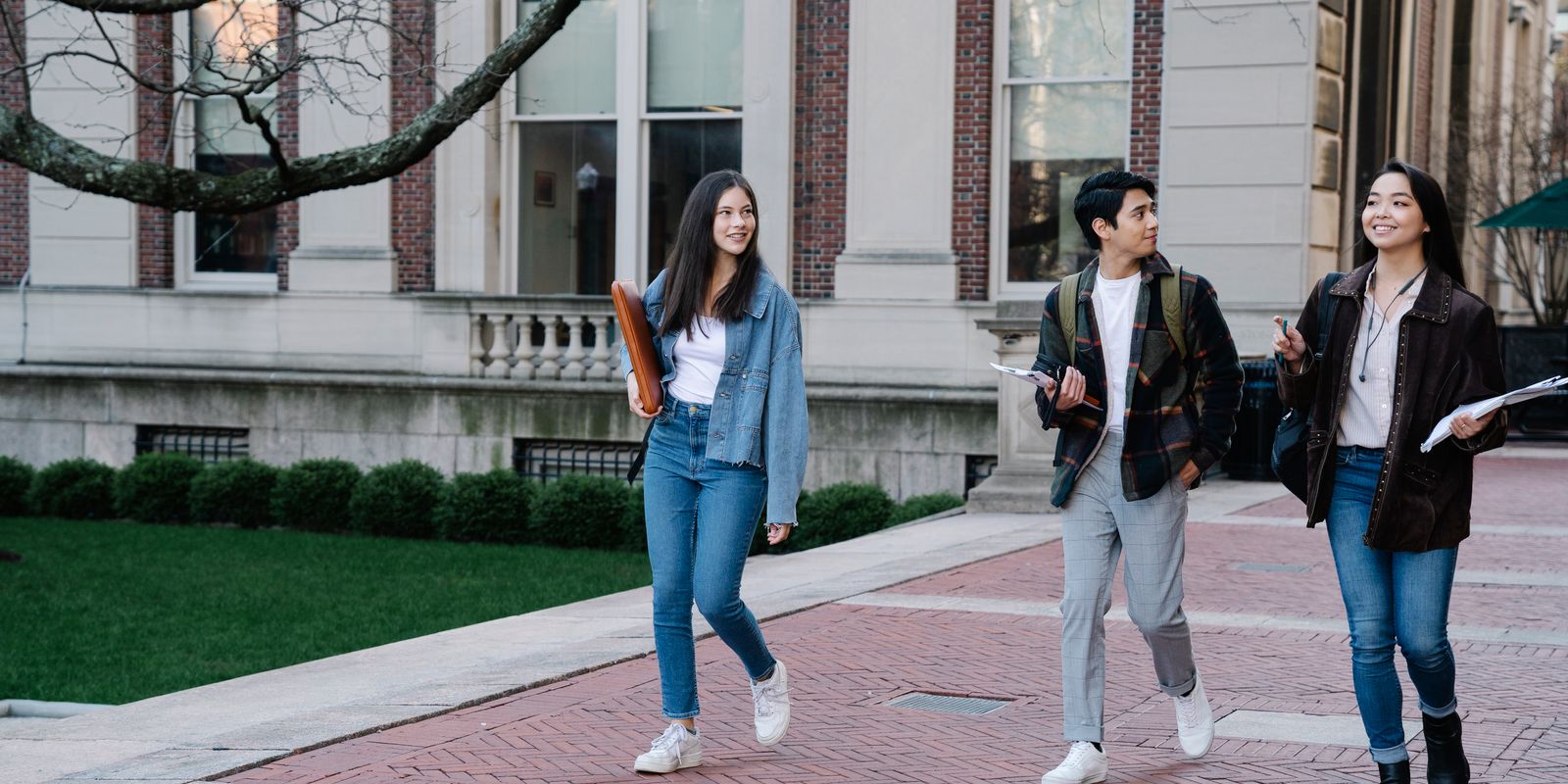 Group of young students walking on campus sidewalk on a bright day, showcasing casual university life.