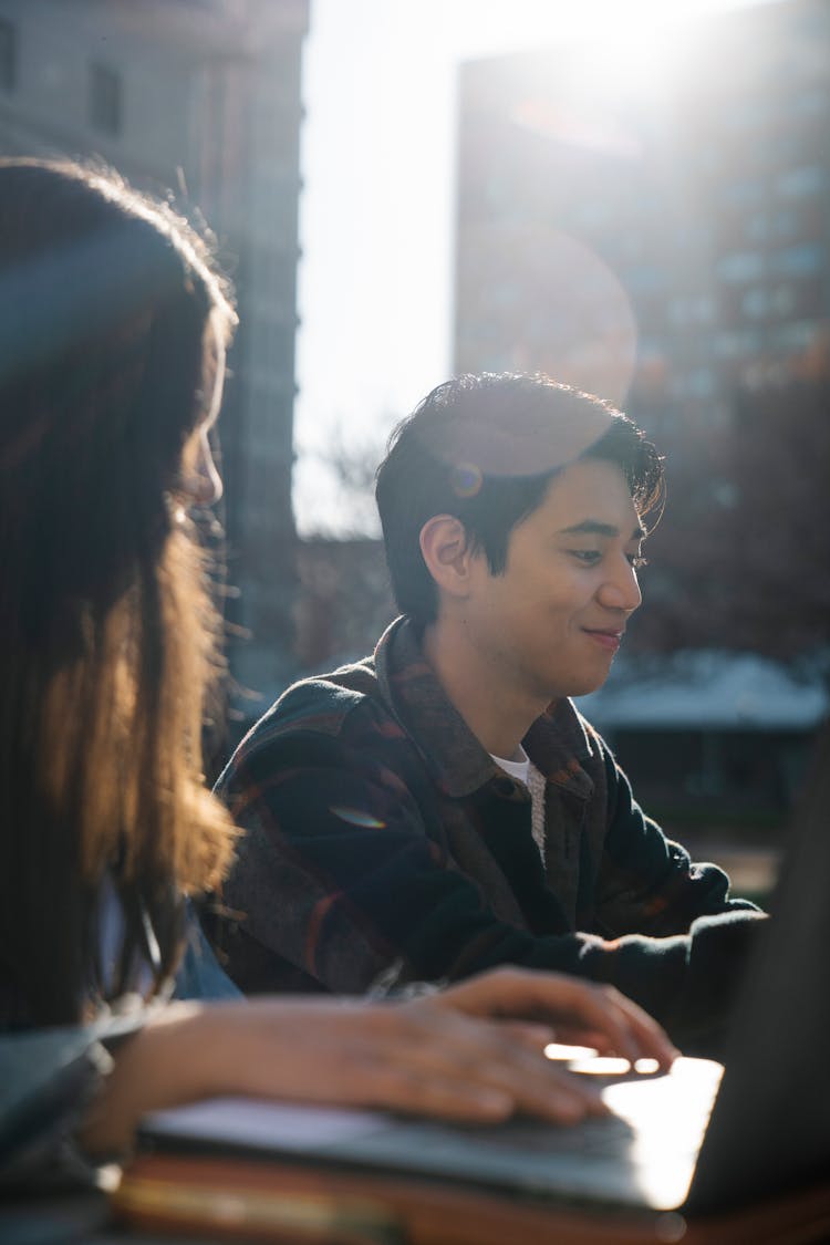 Young Man Smiling And Woman Using Laptop Outdoors In City 