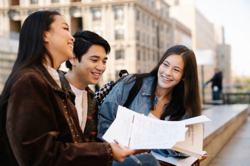 Free Three young adults sitting on campus benches, enjoying their conversation. Stock Photo