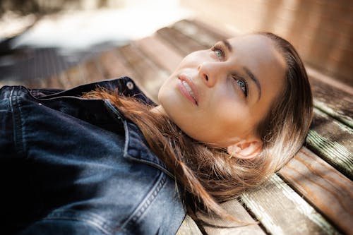 Selective Focus Photo of a Woman in a Denim Jacket Lying on a Wooden Surface