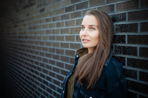 Close-Up Photo of a Beautiful Woman with Brown Hair Leaning on a Brick Wall