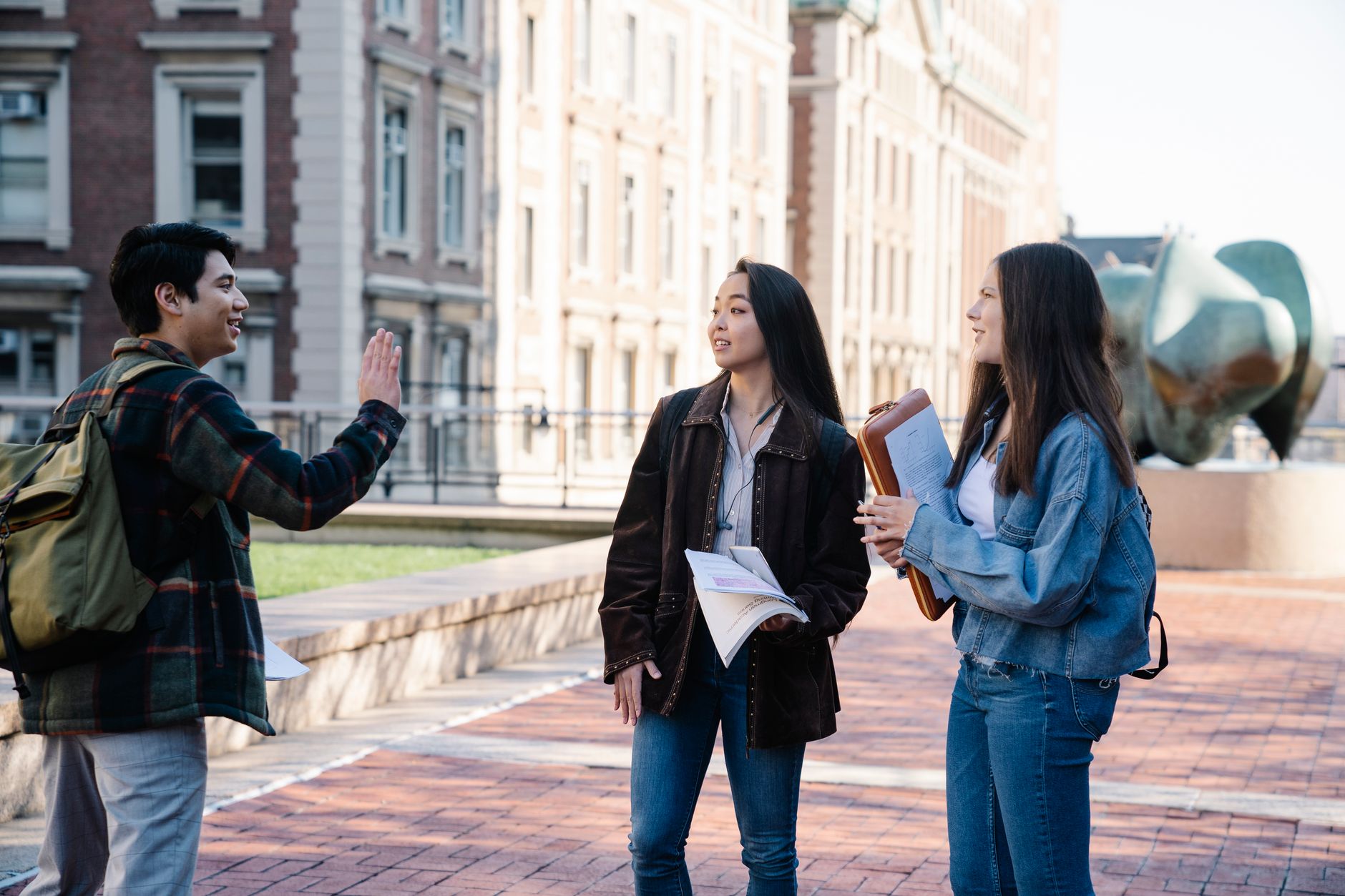 Three university students conversing on a campus sidewalk during the day.