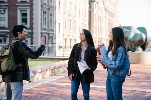 Free Three university students conversing on a campus sidewalk during the day. Stock Photo
