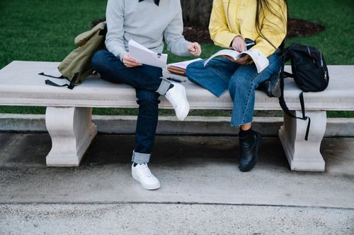 Free Two students studying outdoors on a concrete bench with books and bags. Stock Photo