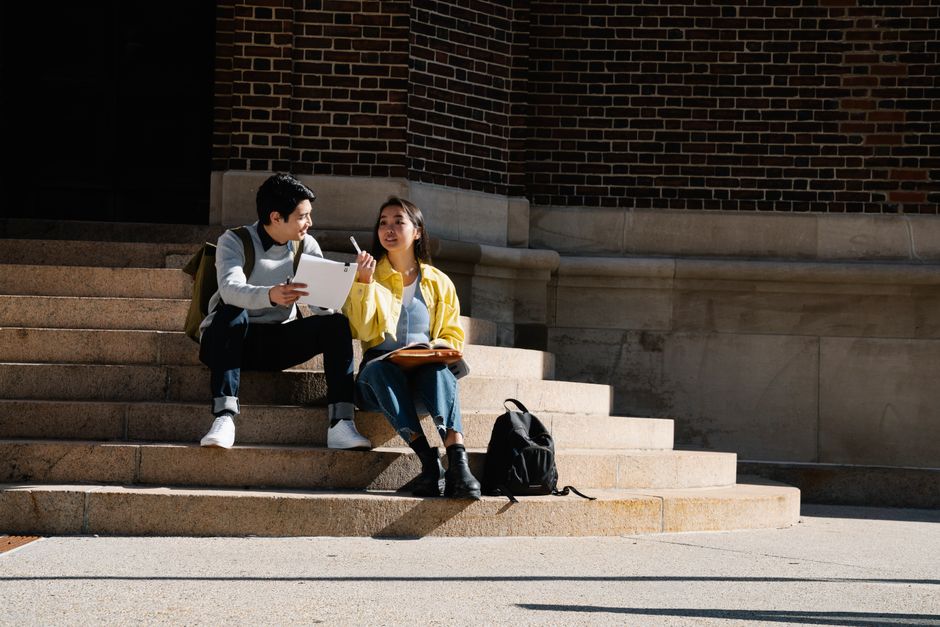 自然光の中で一緒に勉強している2人の大学生が外の階段に座っています。
