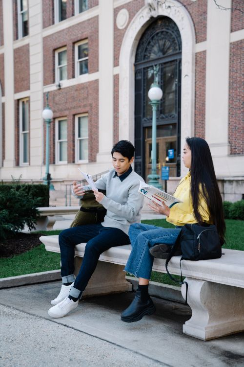 Free Two students studying on a campus bench, surrounded by university architecture. Stock Photo