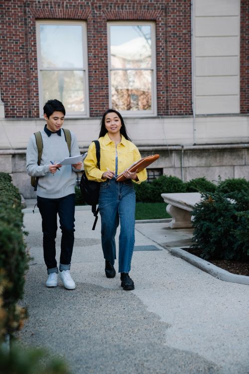 Free Young students walking on university campus, engaging in discussion. Stock Photo