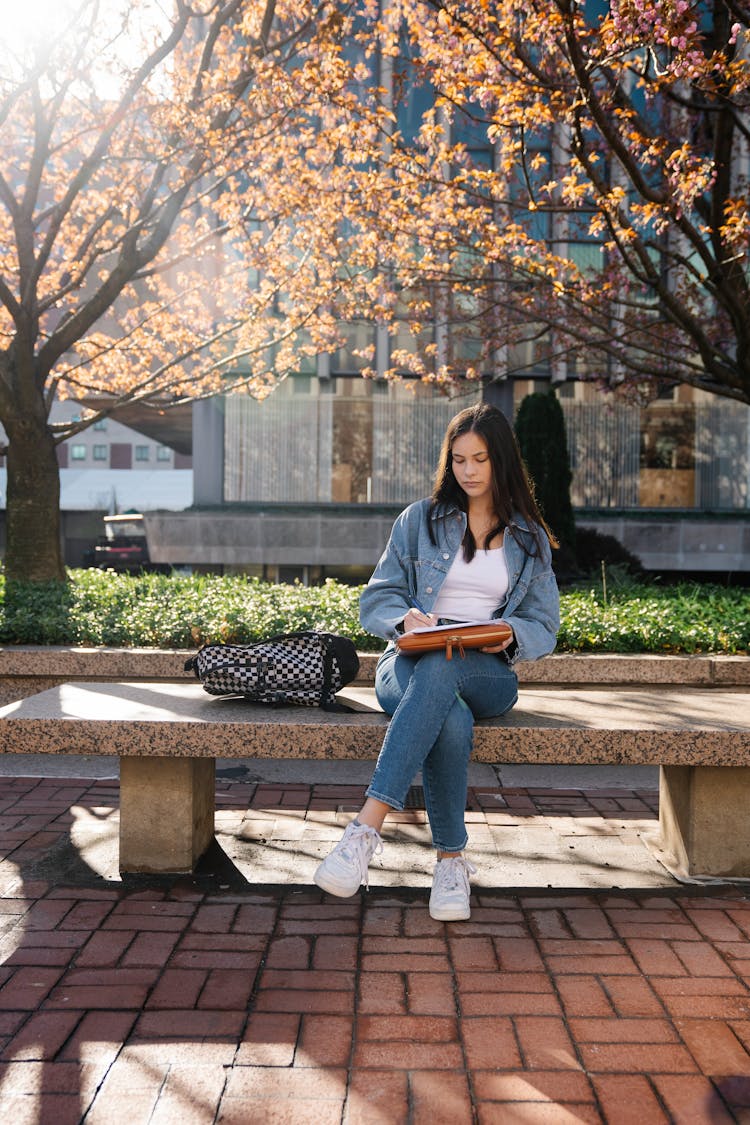 College Student Sitting Outdoors With A Notebook 