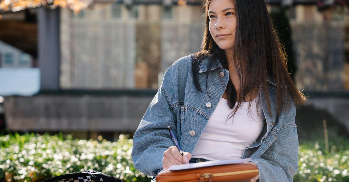 college student sitting alone on a bench on campus at sunset, looking pensive