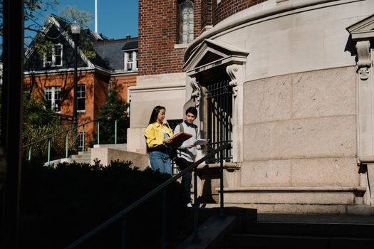 Two students conversing outside a campus building on a sunny day.
