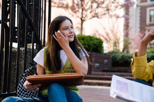 Free Young woman sitting outdoors on campus with a smile during springtime. Stock Photo