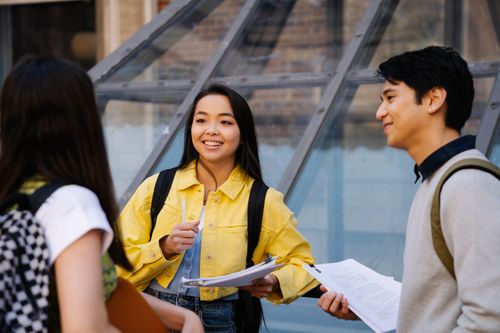 Free Three students conversing with papers in an outdoor setting, sharing ideas and knowledge. Stock Photo