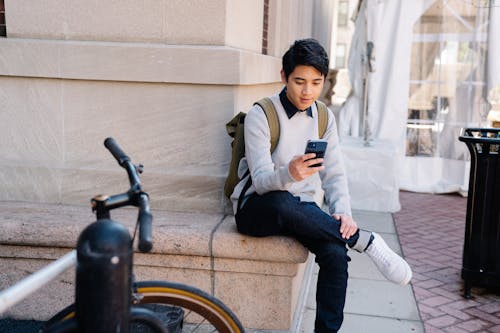 Man in a Gray Sweatshirt Using His Black Cell Phone