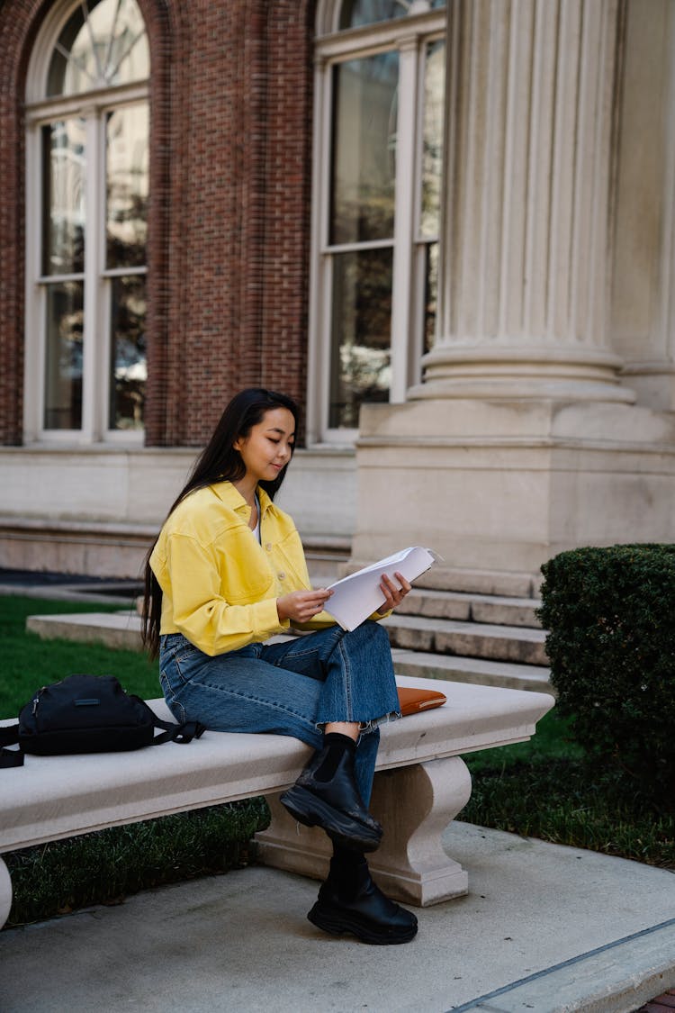 College Student Sitting In Front Of A Building On A Bench And Looking At Her Notes 