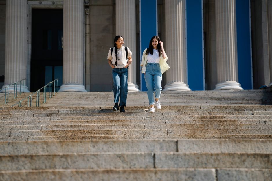 明るい空の下、記念碑的な建物の石の階段を幸せそうに降りる二人の女性。