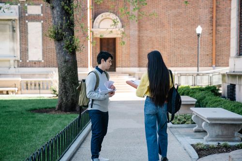 Free Two students talking outside on a university campus path, carrying backpacks and papers. Stock Photo