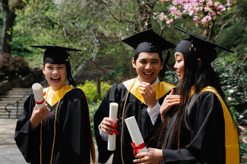 Free Group of diverse students celebrating graduation with diplomas outdoors. Stock Photo
