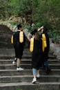 Woman in Black and Yellow Academic Dress Standing on Gray Concrete Stairs