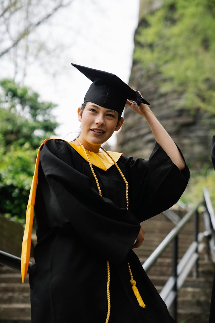 Portrait Of A Young Woman In Mortarboard And Graduation Gown On Steps Outdoors