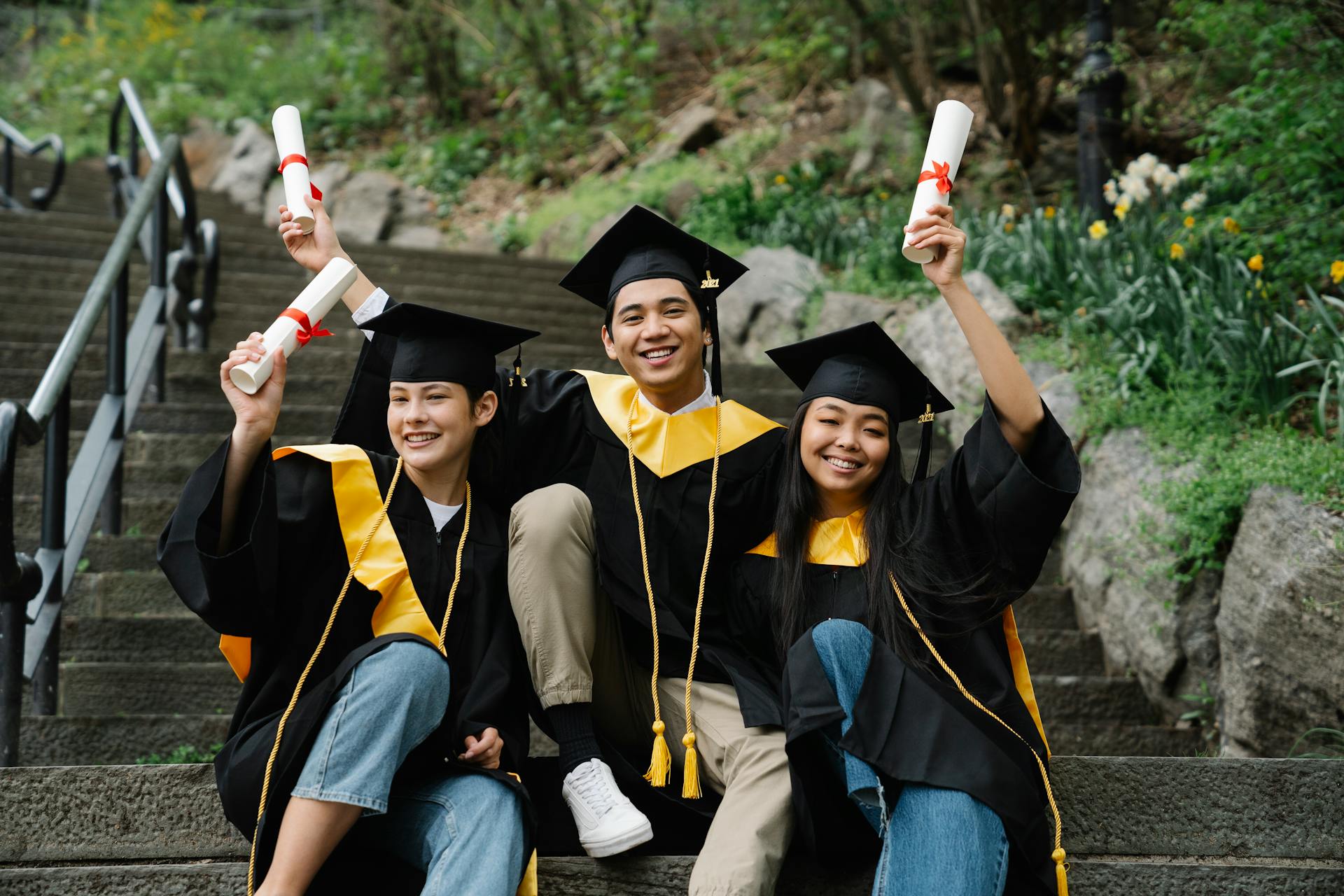 A joyful group of graduates in academic gowns celebrating with diplomas on outdoor steps.