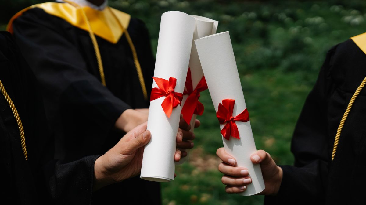 Group of graduates holding diplomas with red ribbons during a ceremony outdoors.