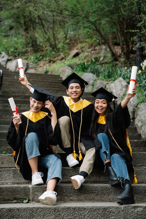 Free Man and Women Sitting on Stairs While Holding Diplomas Stock Photo
