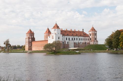 Free Picturesque shot of Mir Castle from across the lake, highlighting its architectural beauty. Stock Photo