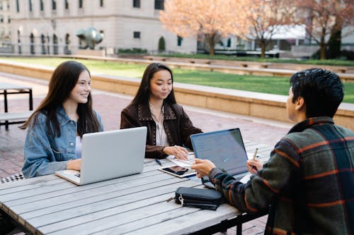 Three Young People Studying Together Outdoors With Laptops