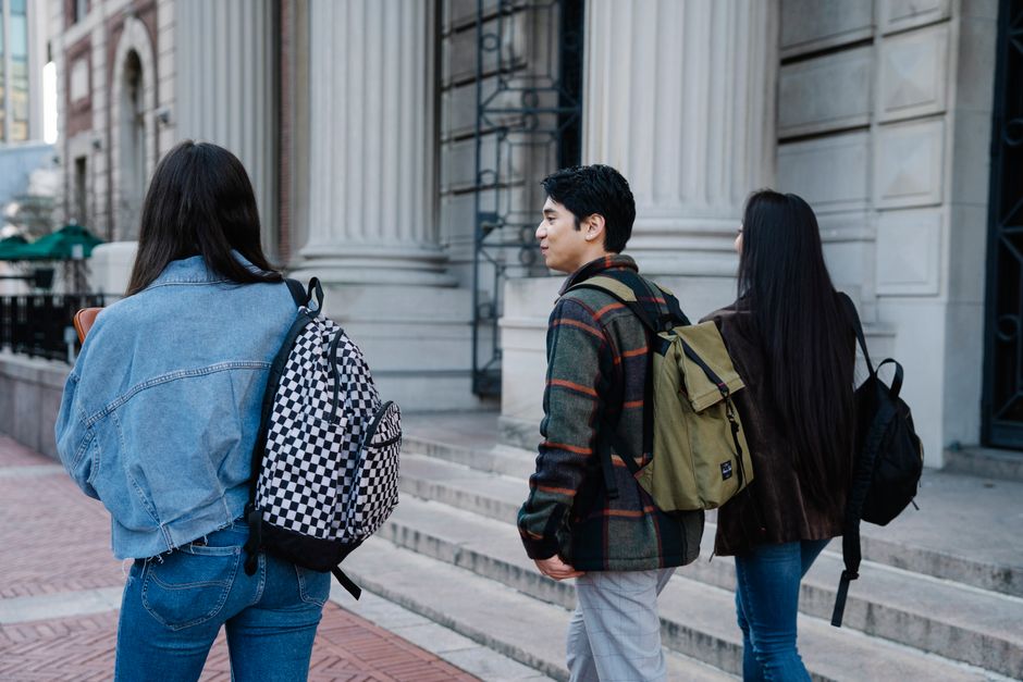 A group of students with backpacks walking past a historic building's columns on a city street.